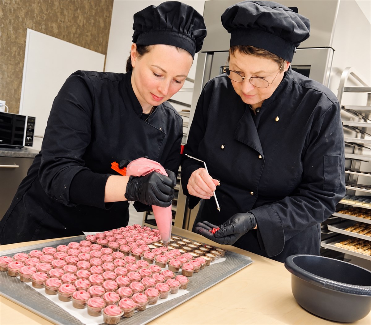 Zwei Frauen verzieren im Atelier Pralinen mit rosa Creme.