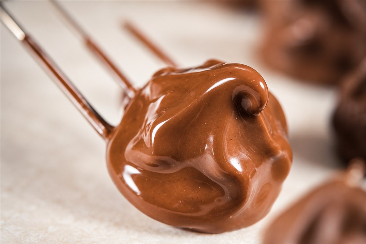 Nahaufnahme einer mit Schokolade überzogenen Praline an einer Pralinengabel